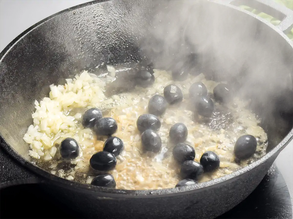 Sautéing diced onions with olives and minced garlic in a cast iron skillet.