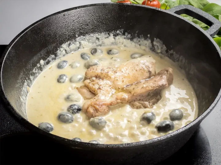 Adding the cooked chicken pieces to the pan with the creamy base of Tuscan chicken.