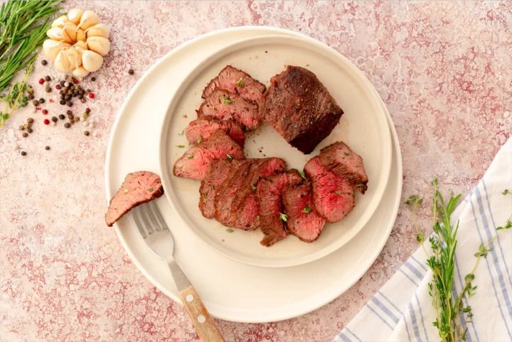 White plate featuring homemade oven-roasted beef tenderloin steaks, with several slices displaying pink centers.
