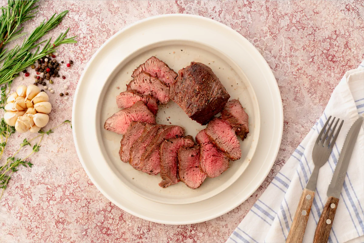 A slice of beef tenderloin with a pinkish hue, served on a white plate.