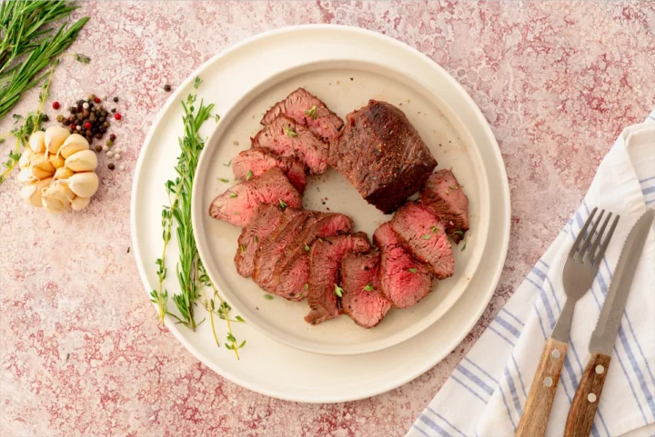 Homemade oven-roasted beef tenderloin sliced displaying its pinkish center, on a white plate.