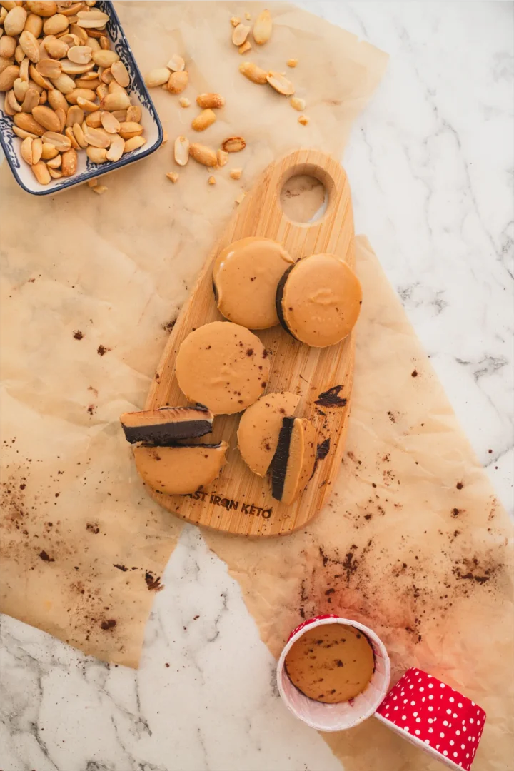 Homemade keto peanut butter cups on a wooden board alongside a small tray of peanuts.