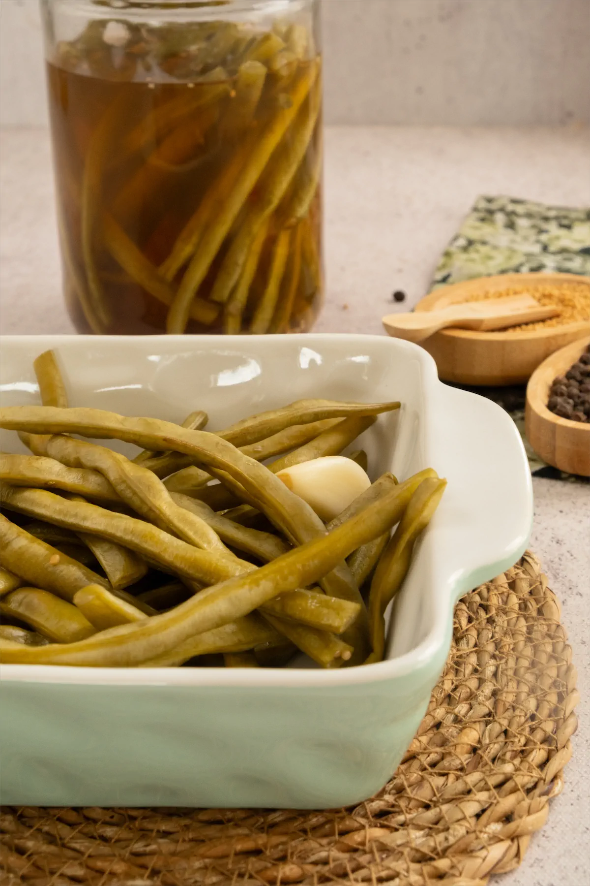 Homemade green bean pickles served in a square white bowl alongside the jar of same pickles.