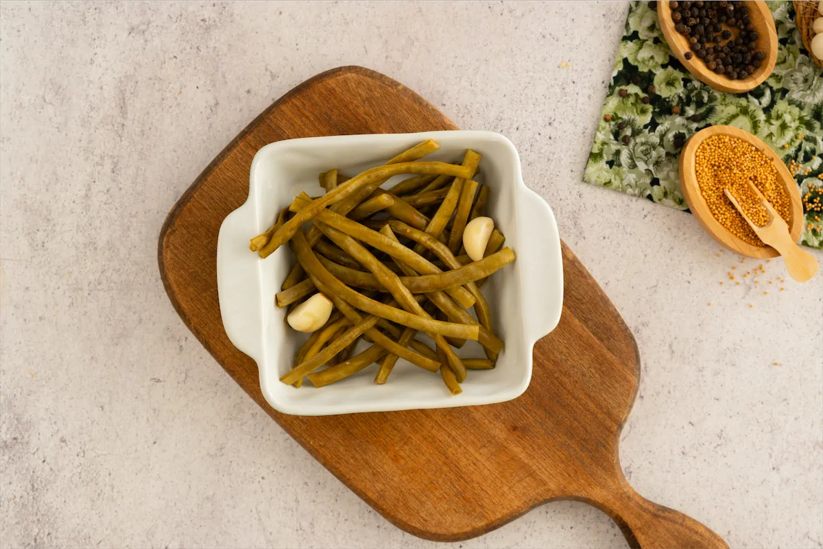 Pickled green beans are presented in a bowl with two garlic cloves
