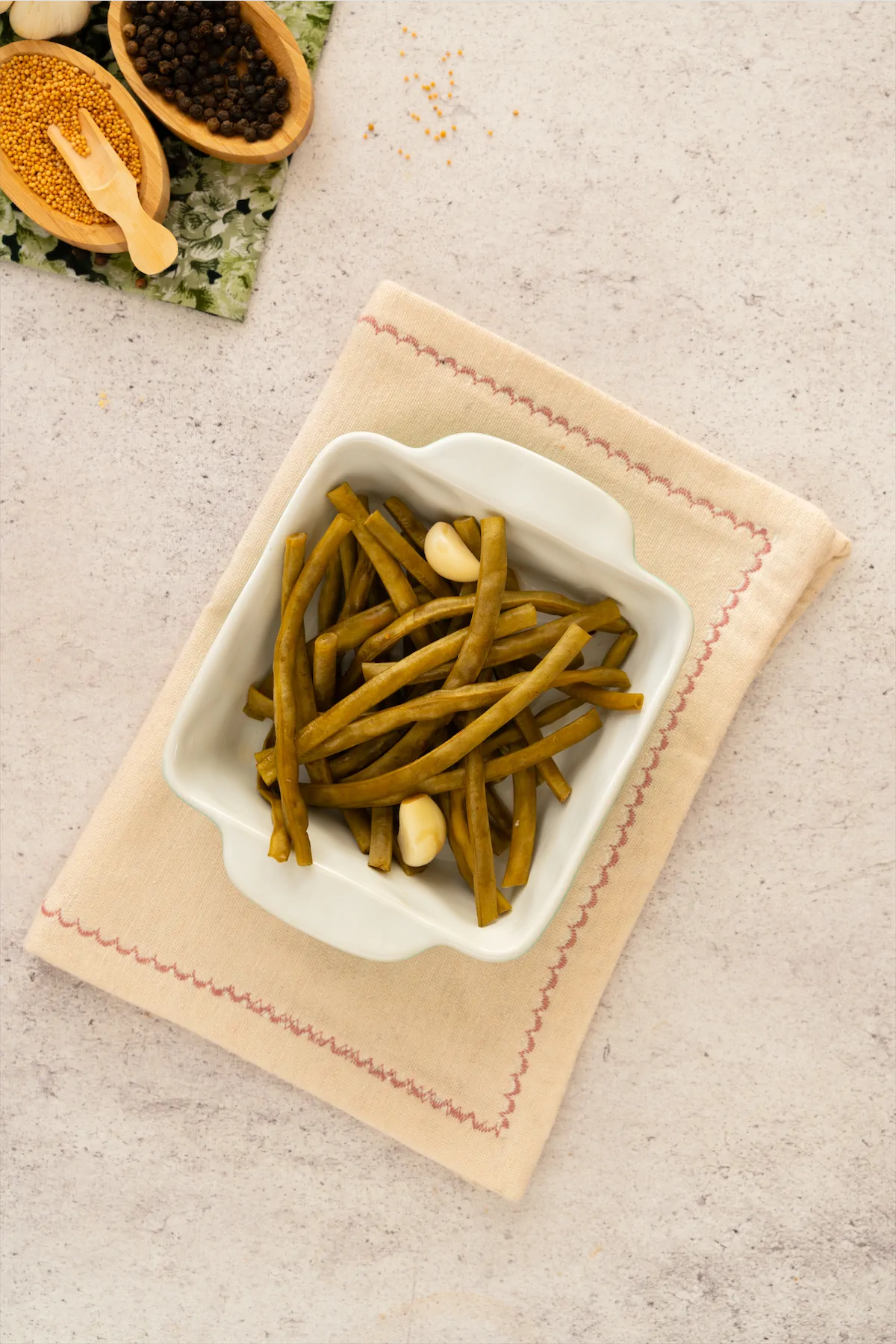 Homemade pickled green beans and a pair of garlic cloves presented in a square white bowl.