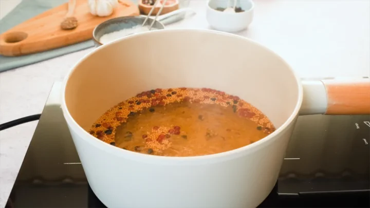 A close-up shot of brine simmering in a sauce pan on an induction top.