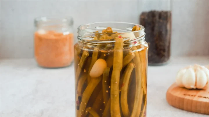 Green beans and garlic with hot brine in a glass jar.