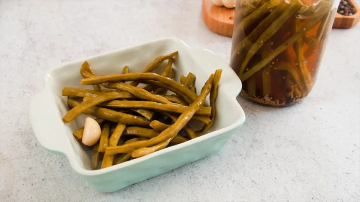 Pickled green beans served in a square white bowl.