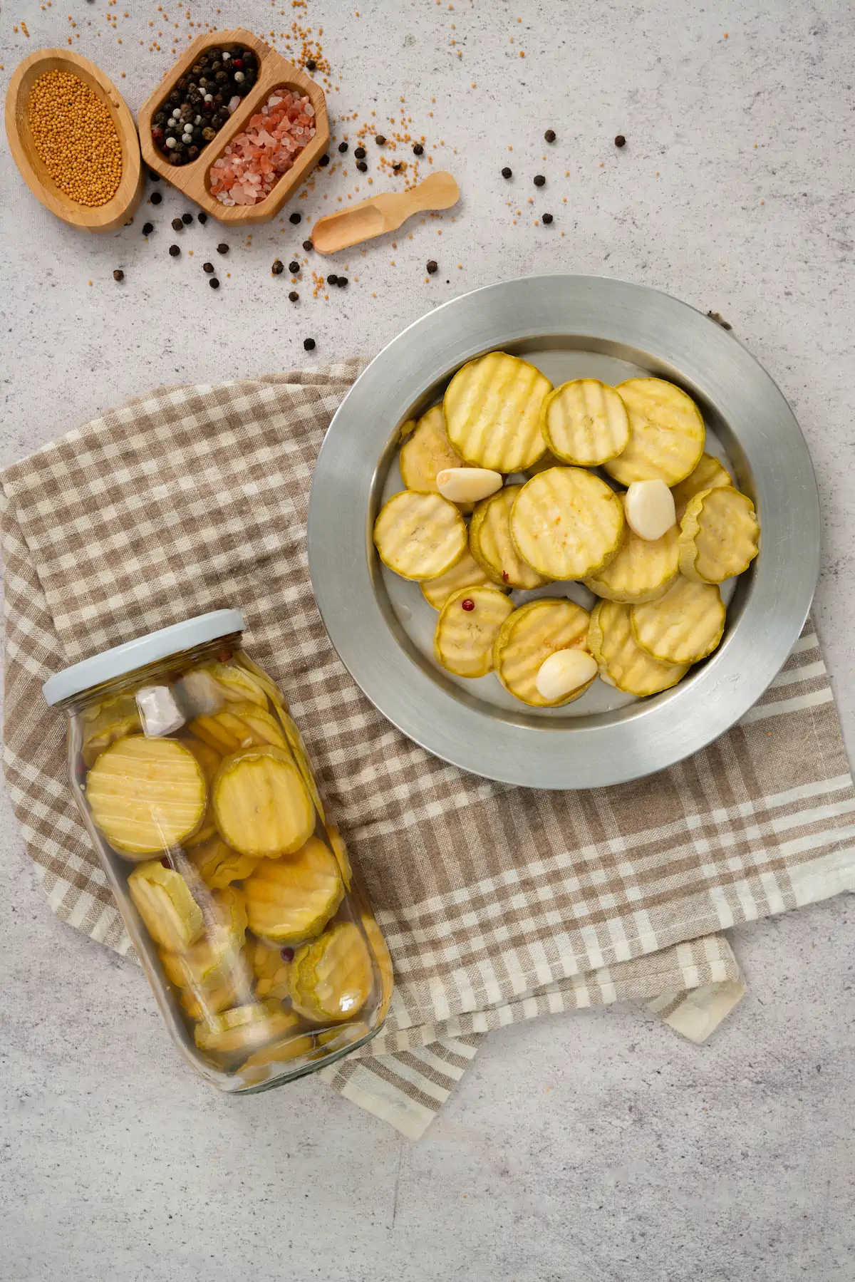 Sliced zucchini pickles served on a plate alongside a jar of the same pickles.