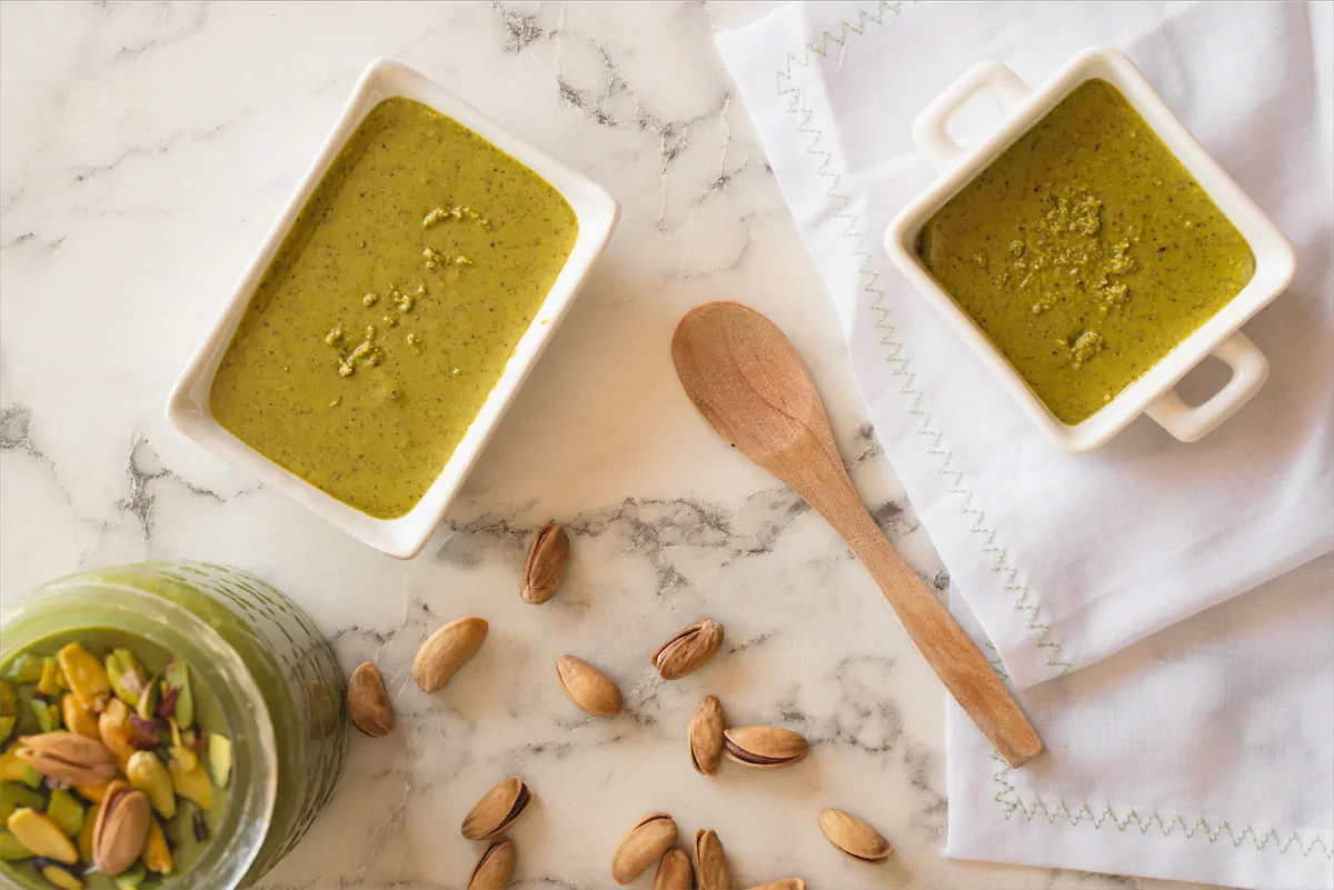 Low-carb pistachio butter in three containers, with one container garnished using pistachio nuts.