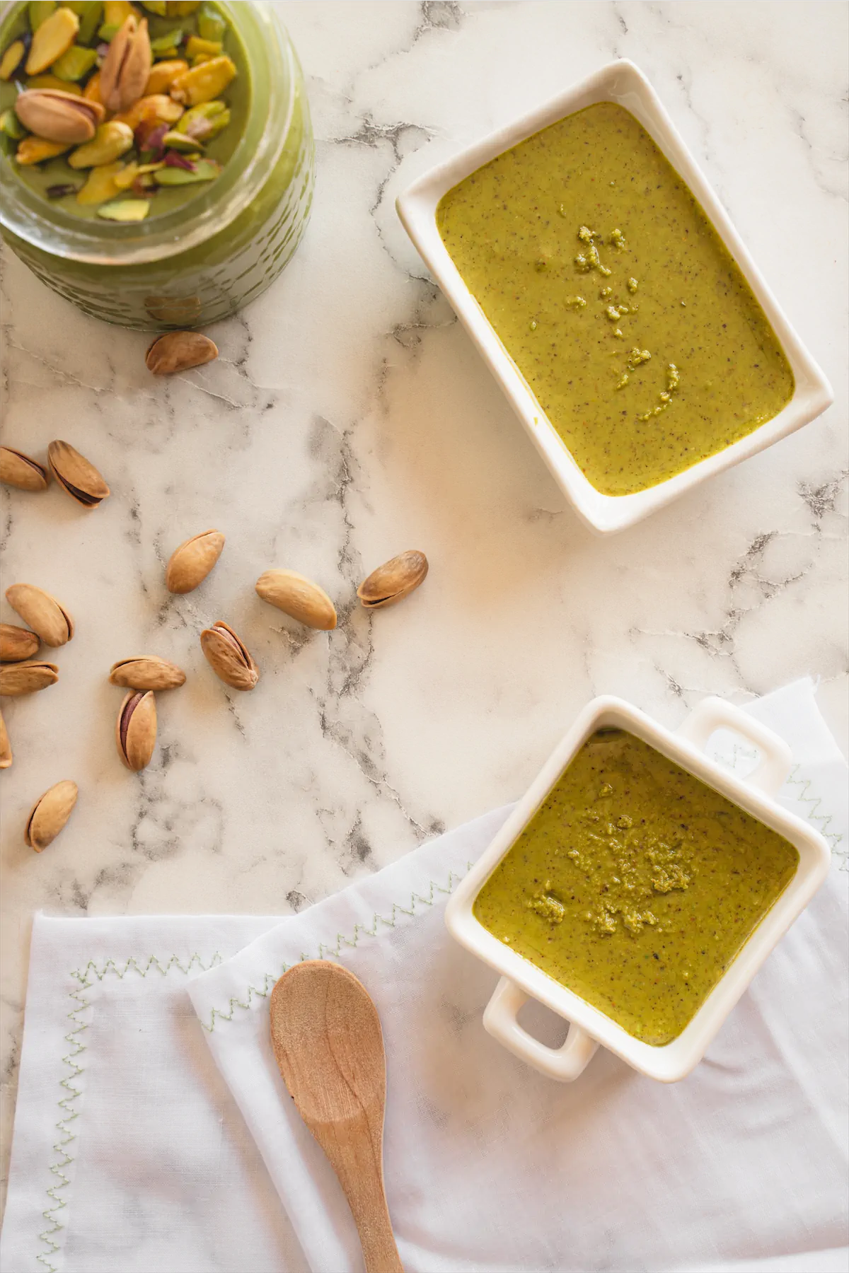 Showcasing sugar-free pistachio butter in three containers, while one is tastefully garnished with pistachio nuts.