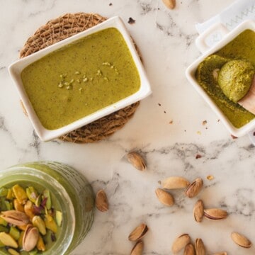 Homemade sugar-free pistachio butter in three containers, with a pistachio nut garnish on one.