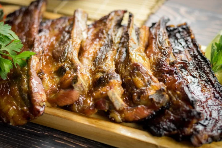 Smoked pork ribs artfully arranged on a wooden plate with fresh herbs.