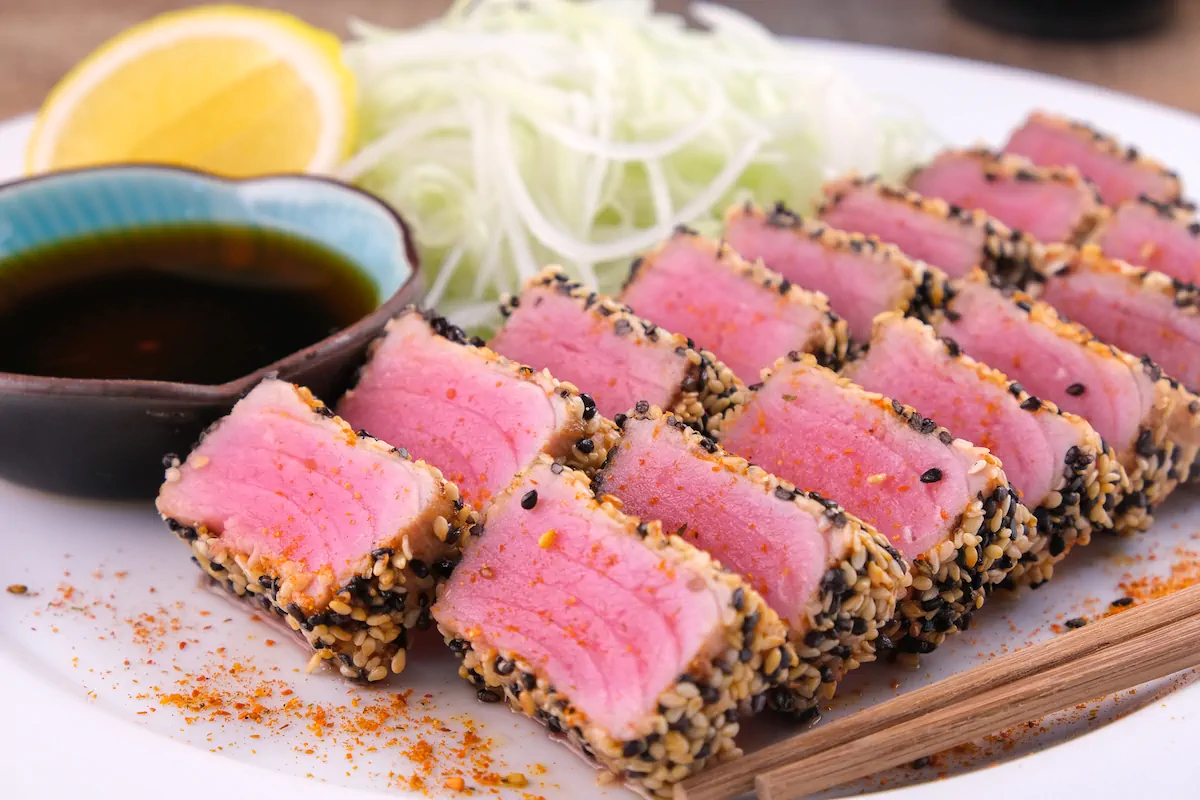 Slices of keto ahi tuna steak with a crispy sesame coating, accompanied by ponzu sauce.