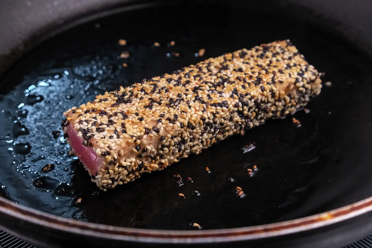 Pan-searing ahi tuna steak coated with sesame seeds in a skillet.