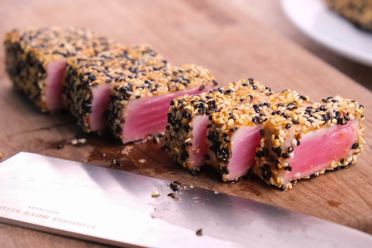 Slicing homecooked ahi tuna steak with a knife on a cutting board.