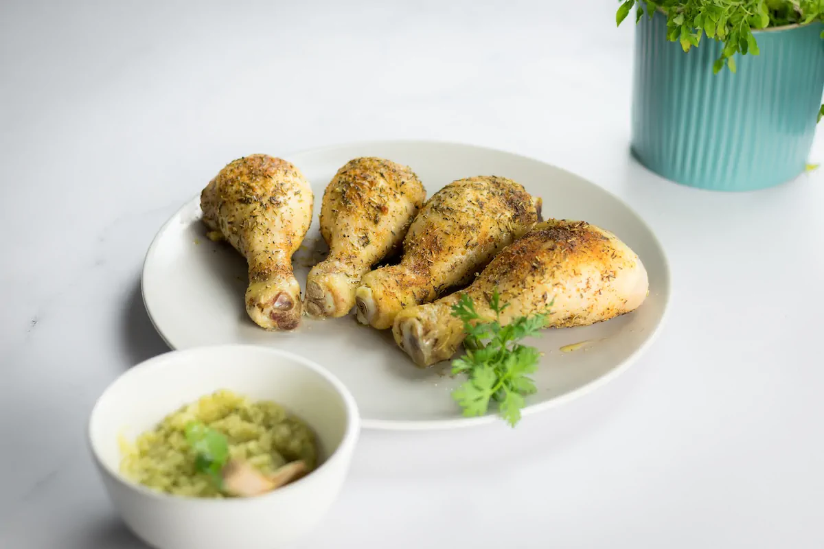 Keto baked chicken legs seasoned with spices, presented on a plate alongside a bowl of pesto sauce.