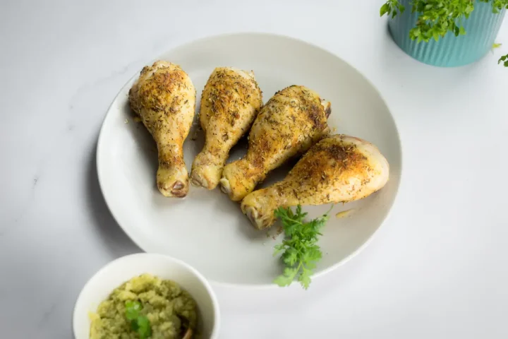 Homemade baked chicken legs with a spice blend served on a plate alongside pesto sauce.