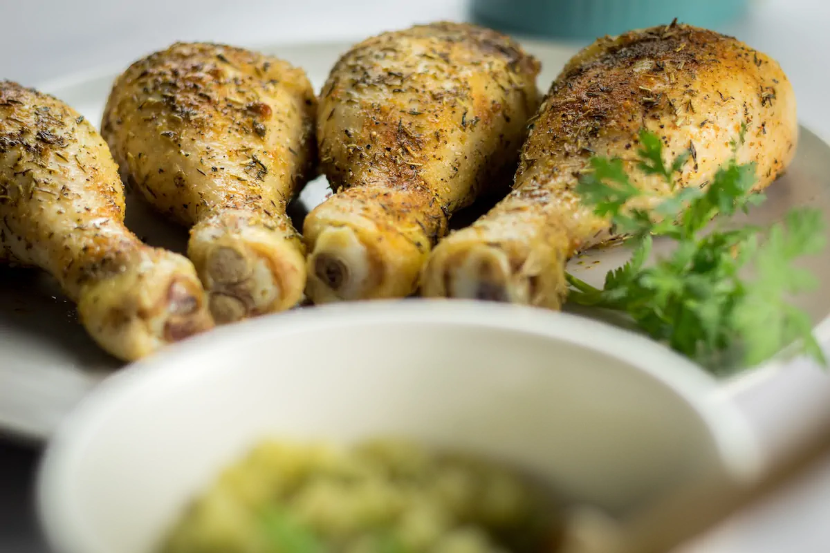 On the plate, keto baked chicken legs, seasoned and baked to perfection, served with a side of pesto sauce.