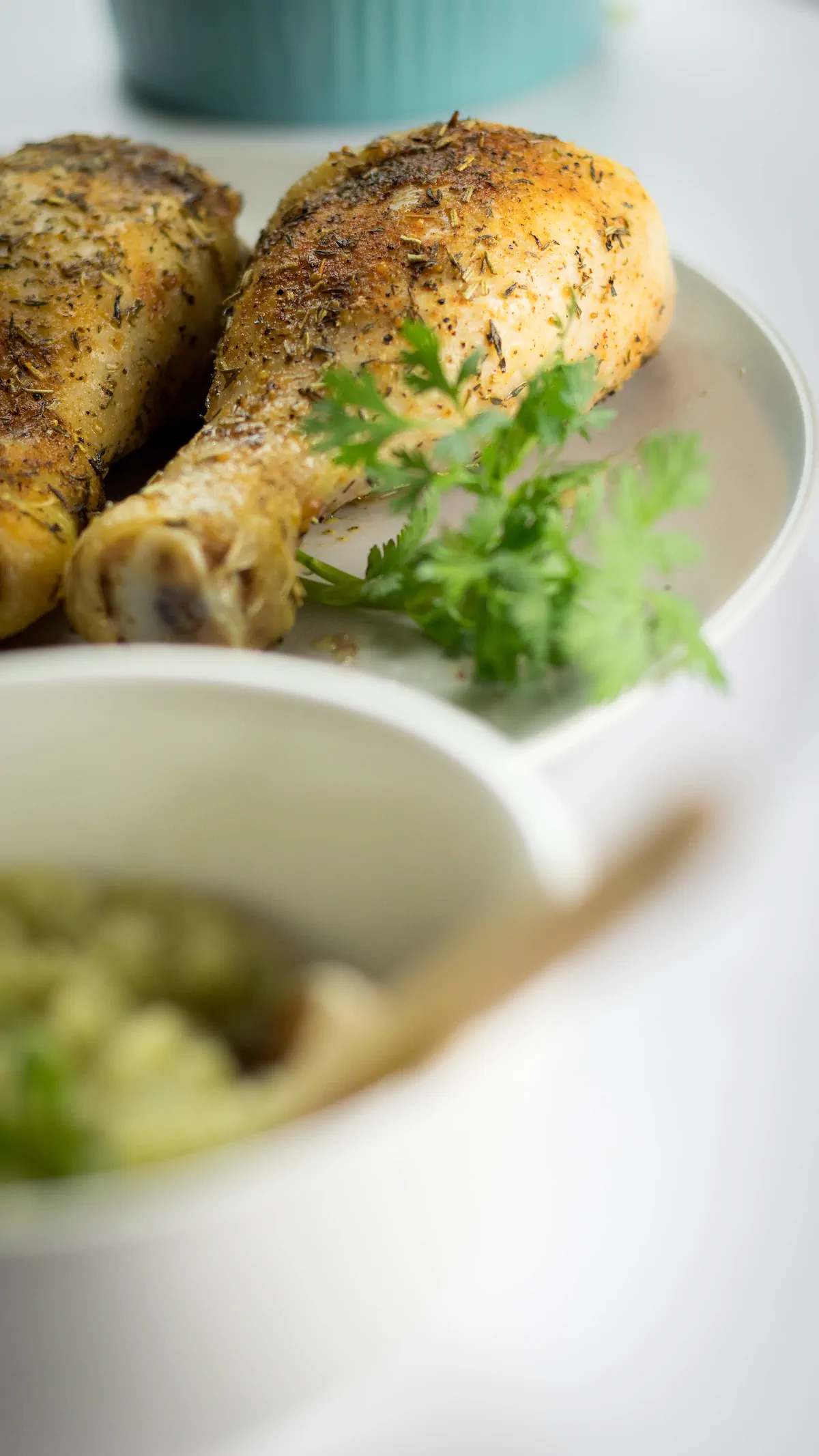 A focused shot of chicken legs baked in the oven and garnished with fresh herbs on a plate.