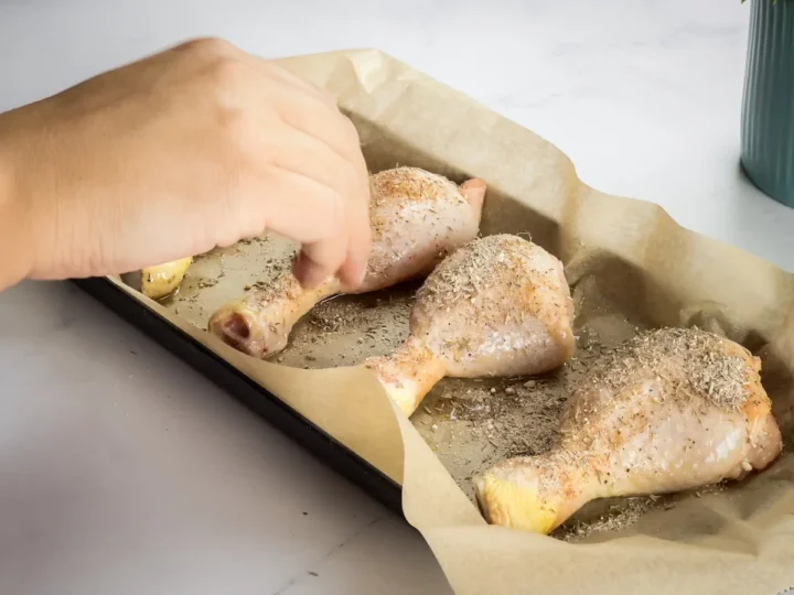 A hand sprinkling the spice rubs onto the chicken thighs with oil.