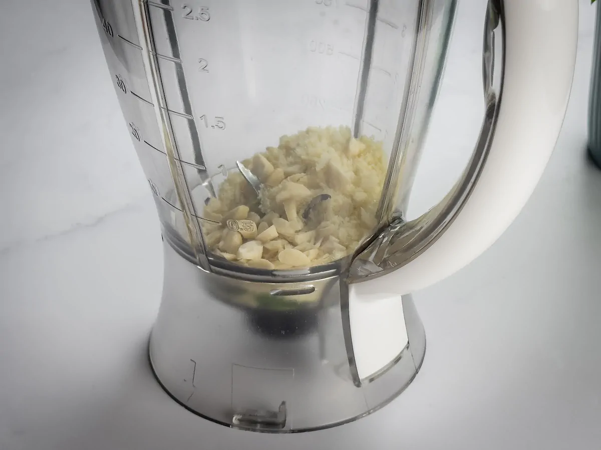 A transparent blender jar with Parmesan cheese, pine nuts, and minced garlic for the pesto sauce.