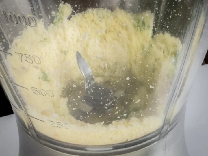 Ingredients for the pesto sauce are blended and seen from a transparent blender jar.