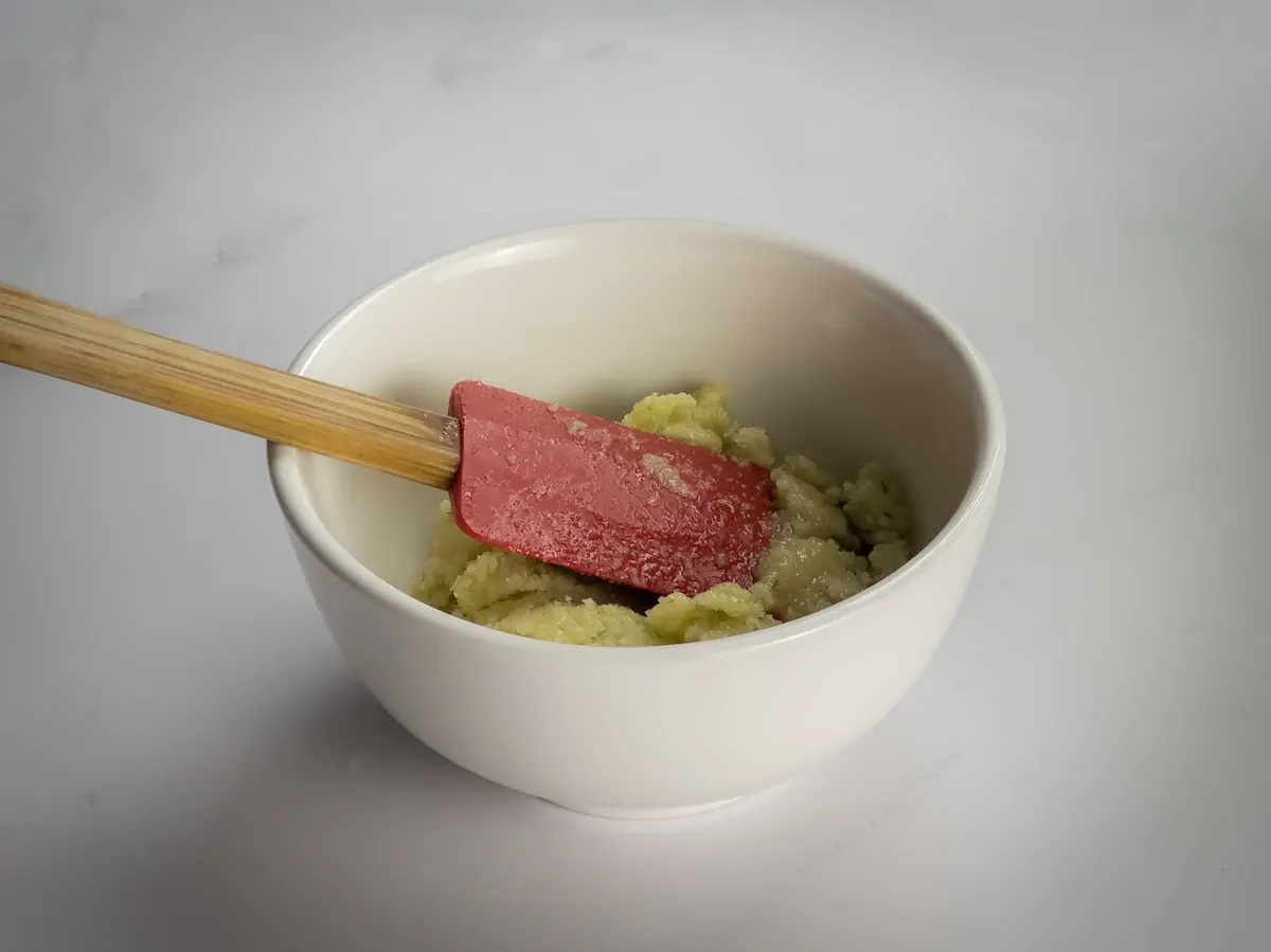 Pesto sauce in a bowl with a silicone spatula.