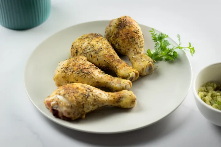 Oven baked chicken legs with spices served on a plate and garnished with fresh herbs.