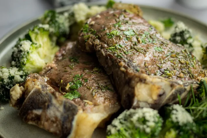Oven-cooked ribeye steak served with cheesy roasted broccoli on a plate.
