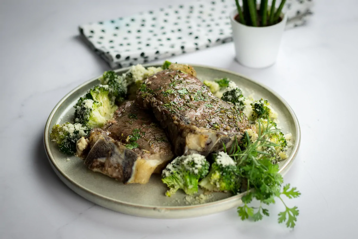 Low-carb baked ribeye steak with cheesy roasted broccoli, presented on a plate and garnished with fresh herbs.