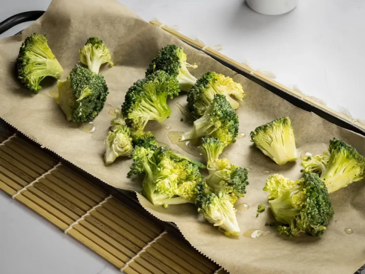 Broccoli florets with olive oil on a baking tray with parchment paper.