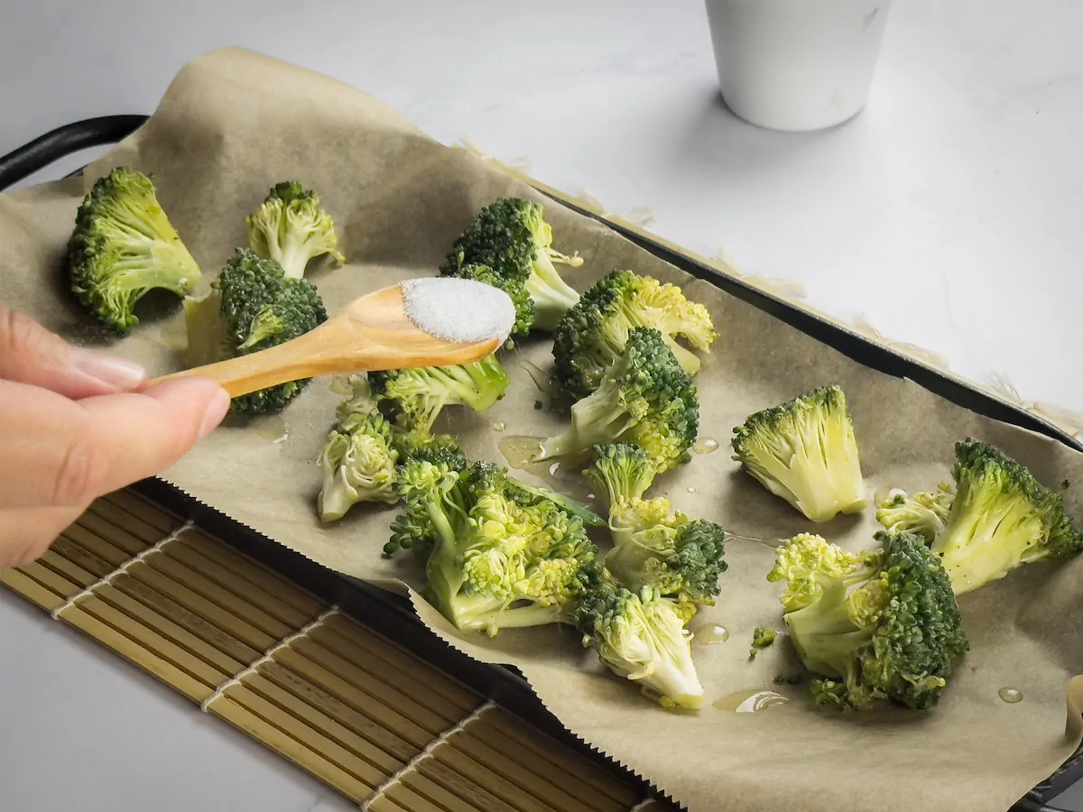Sprinkling salt over the broccoli florets on a baking tray lined with parchment paper.