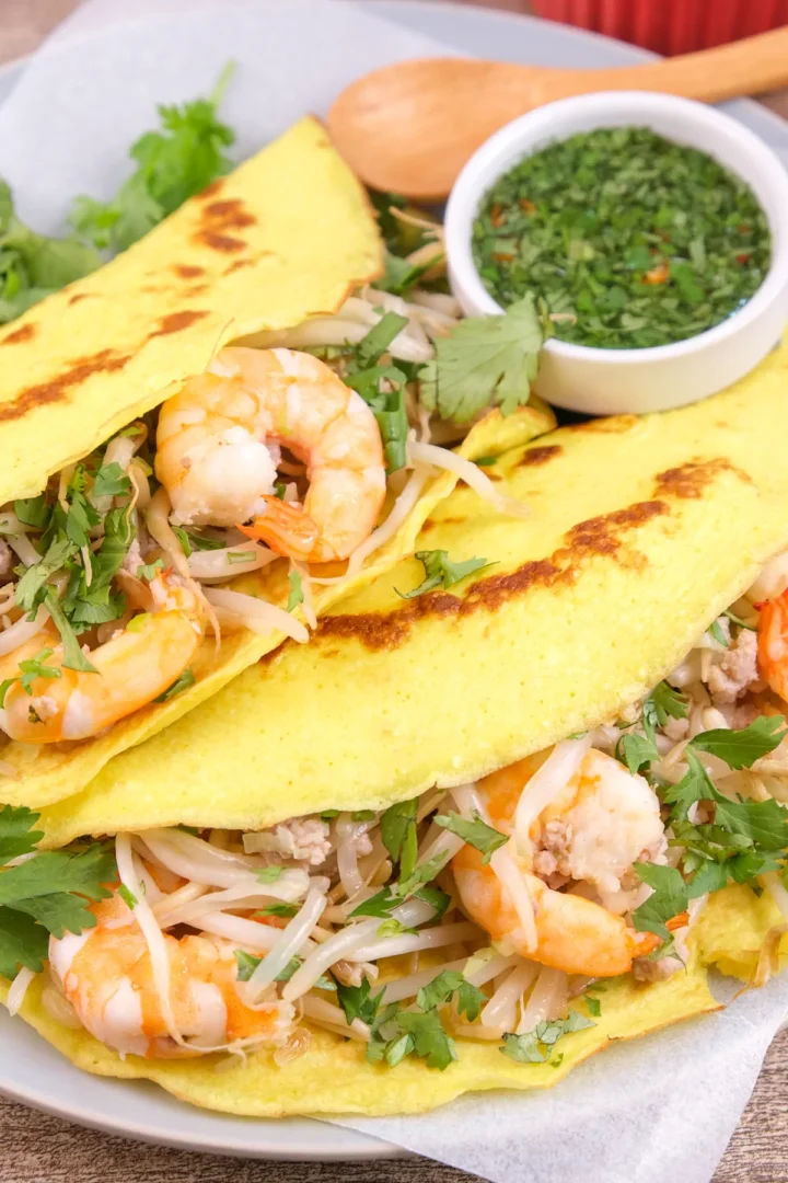 A plate of homemade banh xeo featuring pork and shrimp is served, along with a bowl of dipping sauce.