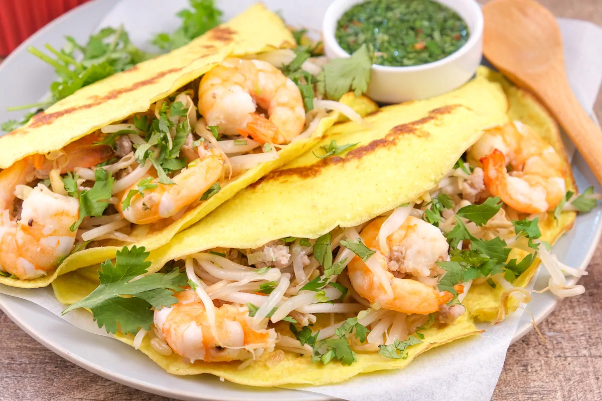 Low-caarb banh xeo with pork and shrimp on a plate, accompanied by a bowl of dipping sauce.