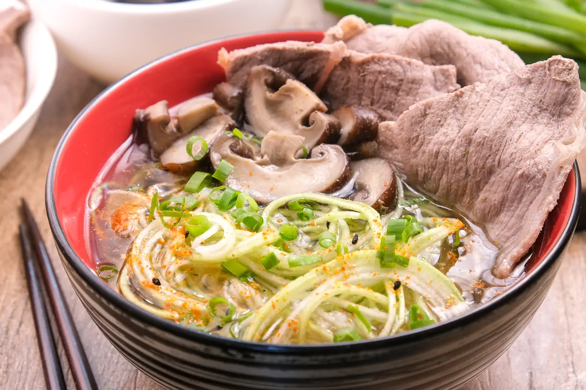 A bowl of homemade beef ramen, featuring slices of beef, zucchini noodles and mushrooms.