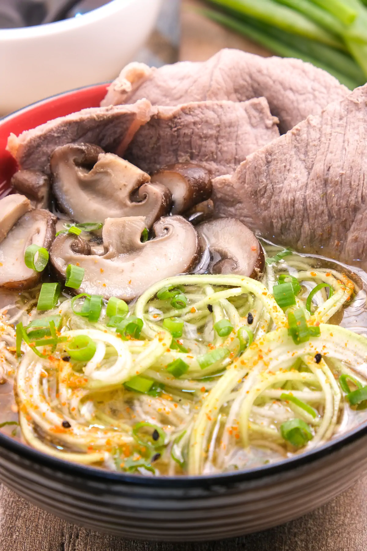A bowl filled with homemade beef ramen, featuring zucchini noodles and mushrooms, and complemented by chopsticks.