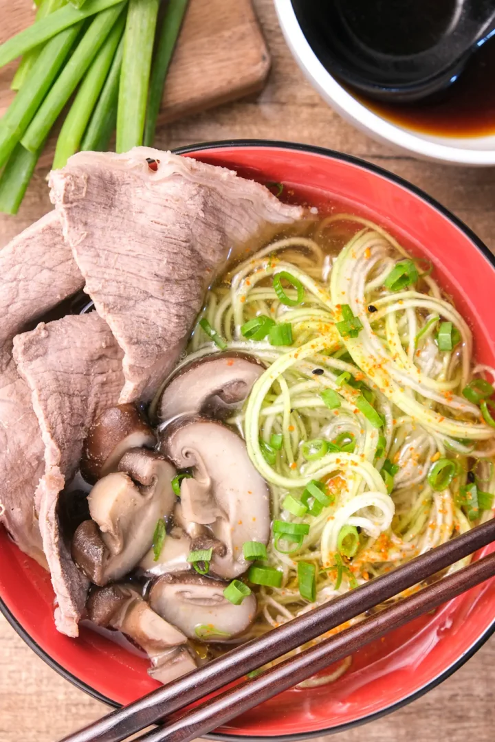 A bowl of homemade beef ramen featuring zucchini noodles and mushrooms, served with chopsticks.