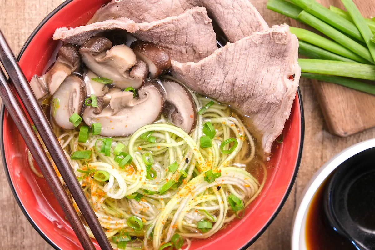 Homemade beef ramen with zucchini noodles and mushrooms in a bowl with chopsticks.