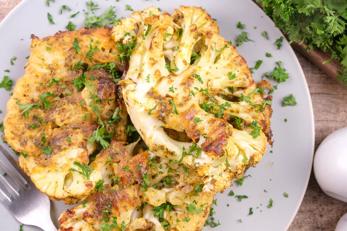 Low-carb golden cauliflower steak served on a plate and garnished with fresh herbs.