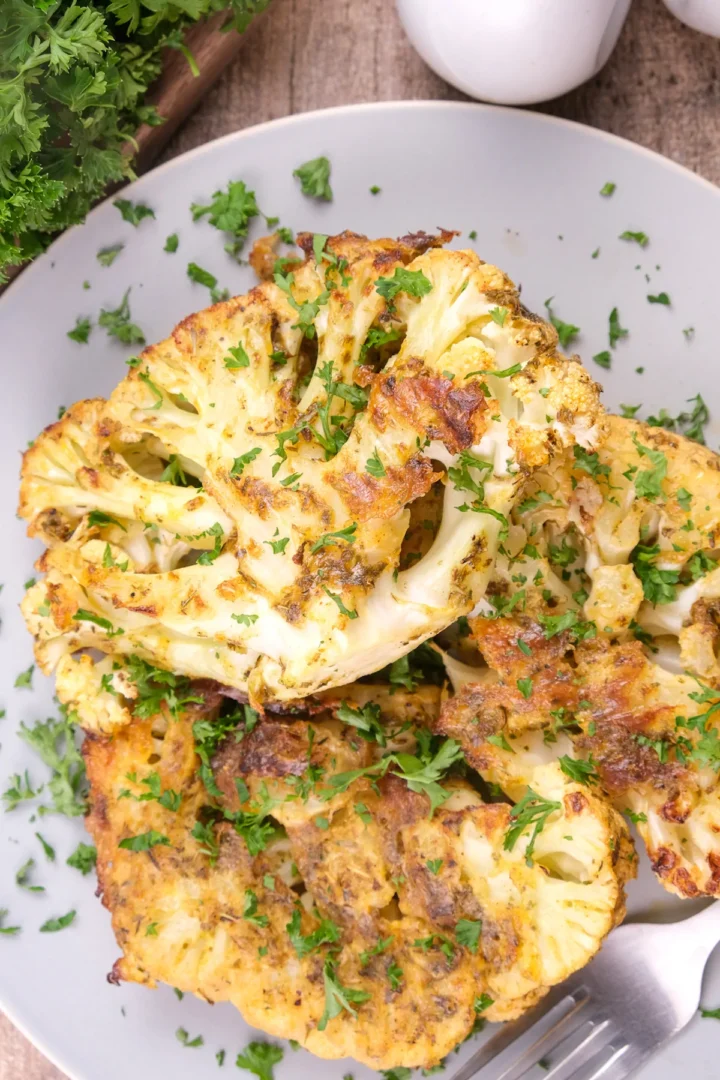 Homemade golden cauliflower steak garnished with fresh green herbs.