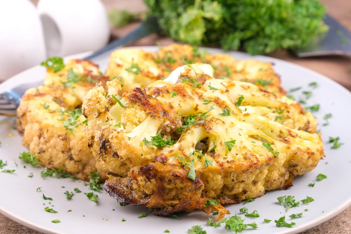 Oven-baked golden cauliflower steak with Creole butter served on a plate and garnished with fresh herbs.