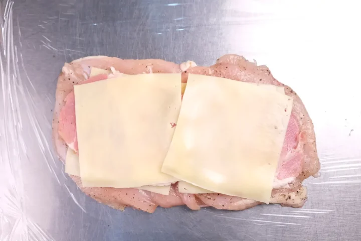 Layering cheese and ham on top of a flattened chicken breast.