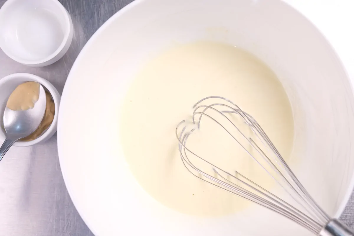 Whisking heavy cream, egg yolk, and Dijon mustard in a bowl.