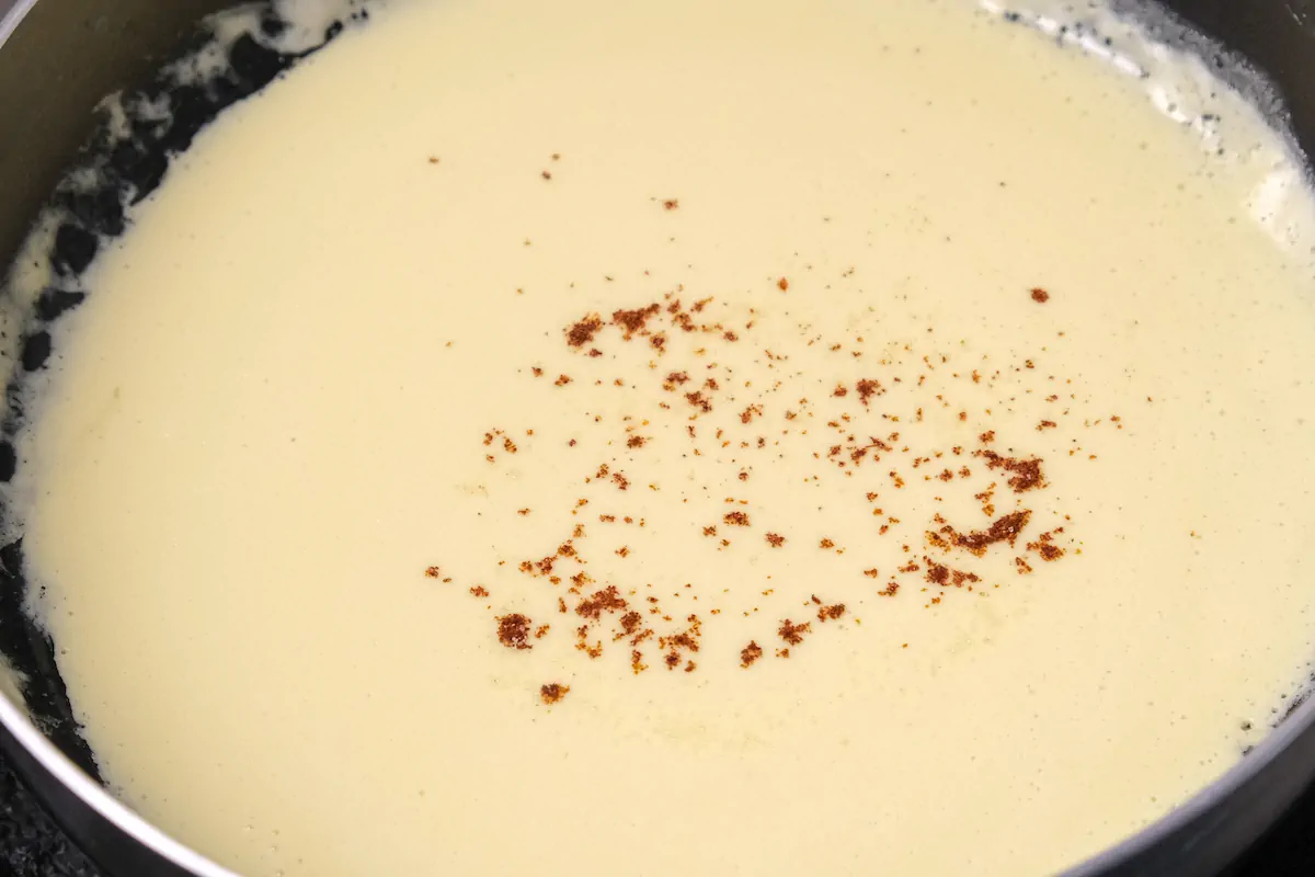 Seasoning the cheesy sauce with salt and cayenne pepper.