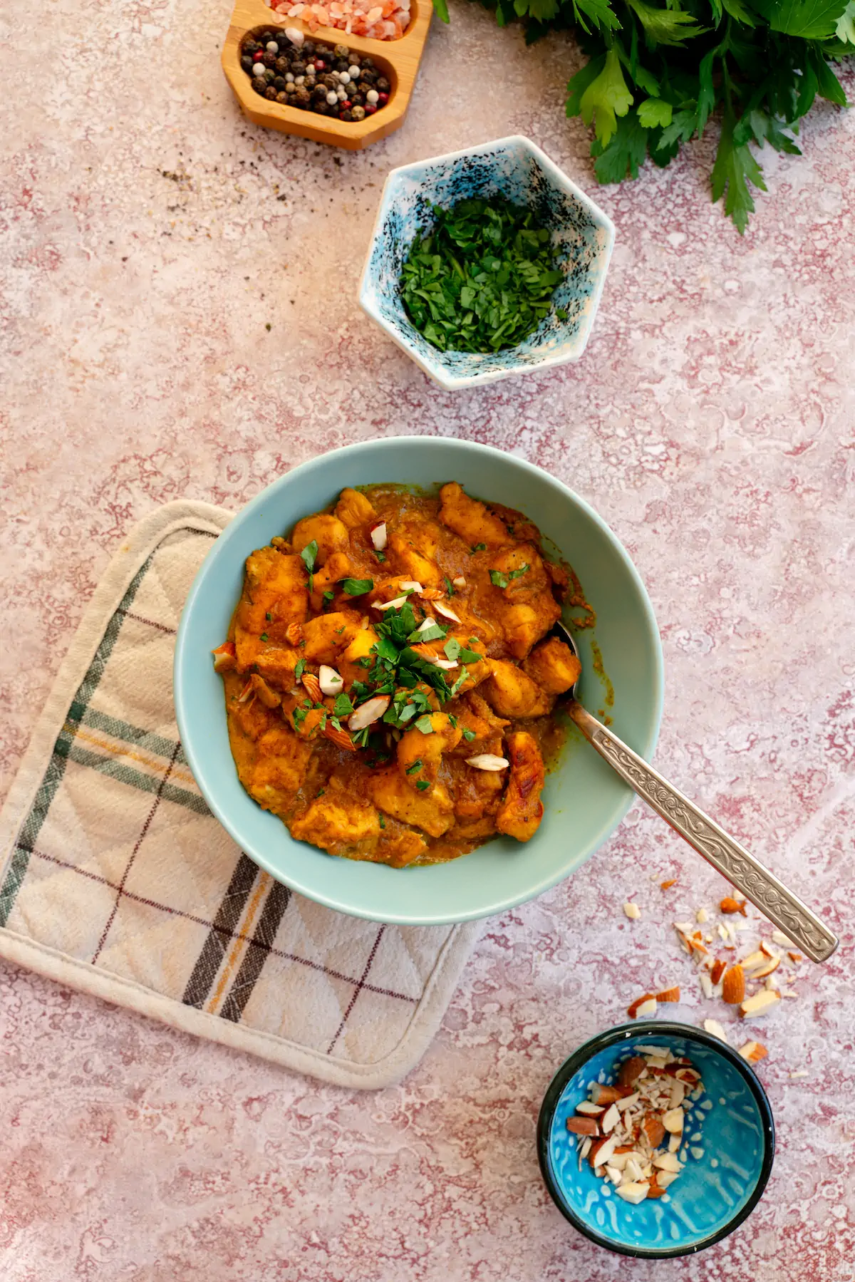 Chicken korma served in a bowl, adorned with almonds and fresh herbs, and accompanied by a spoon.