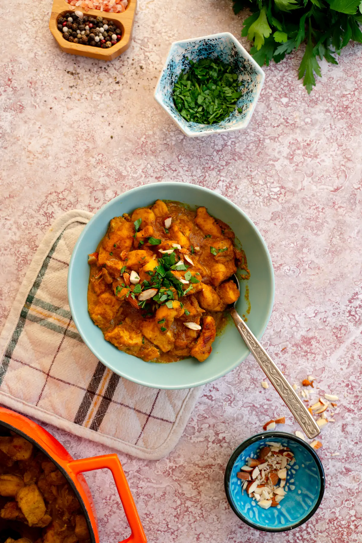 A bowl containing chicken korma, garnished with almonds and fresh herbs, and accompanied by a spoon.