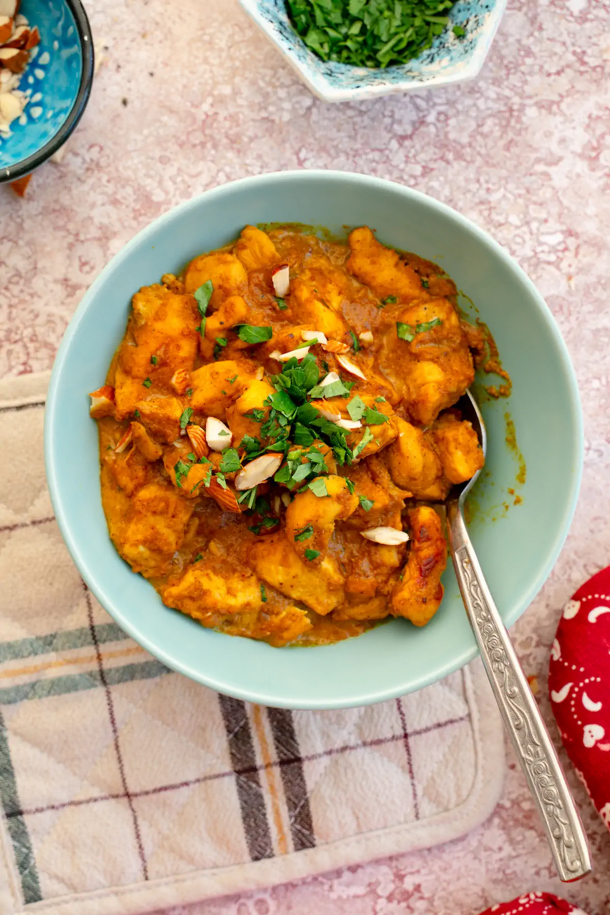 Chicken korma in a bowl, topped with almonds and fresh herbs, and served with a spoon.