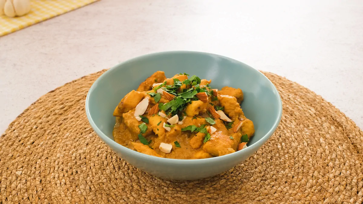 Chicken korma garnished with fresh green herbs and chopped nuts served in a blue bowl.