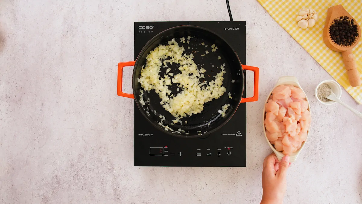 Sautéing chopped onion in coconut oil in a cast iron skillet alongside a bowl of skinless boneless chicken.